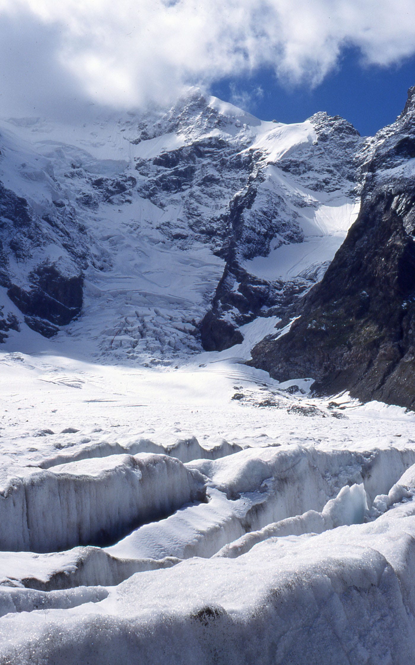 Snow and rock peak, glacier descending to foreground, two tiny figures on it