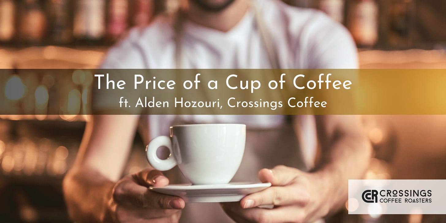 A barista hands a white coffee mug on a matching saucer to the camera. The barista is blurred and cropped at the shoulders and waist.