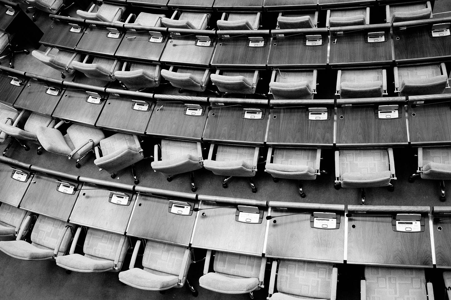 Overhead shot of seating in a parliamentary chamber, in monochrome.