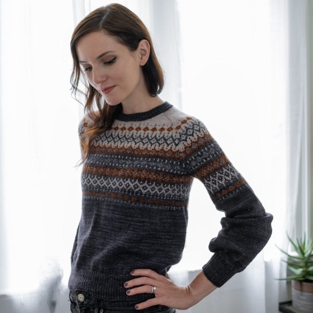 Knitting and Crochet Projects 2023: Hand-knitted Kismet Sweater by Rachel Illsley, featuring intricate colorwork in Voolenvine Yarns. The main color is a dark, shaded black called 'Grimm,' with accents in golden brown and slate gray. The sweater showcases beautiful Raglan shaping and a detailed yoke pattern, knitted by Kristin Lehrer. Knitting and Crochet Projects 2023: Hand-knitted Kismet Sweater by Rachel Illsley, featuring intricate colorwork in Voolenvine Yarns. The main color is a dark, shaded black called 'Grimm,' with accents in golden brown and slate gray. The sweater showcases beautiful Raglan shaping and a detailed yoke pattern, knitted by Kristin Lehrer.