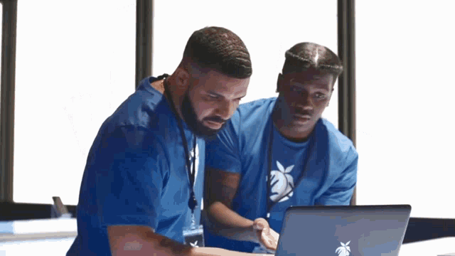 two men in blue shirts are looking at an apple laptop two men in blue shirts are looking at an apple laptop