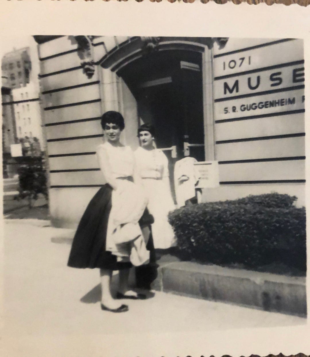 Two young women in dresses hold jackets and bags in from the of a building labeled Guggenheim.