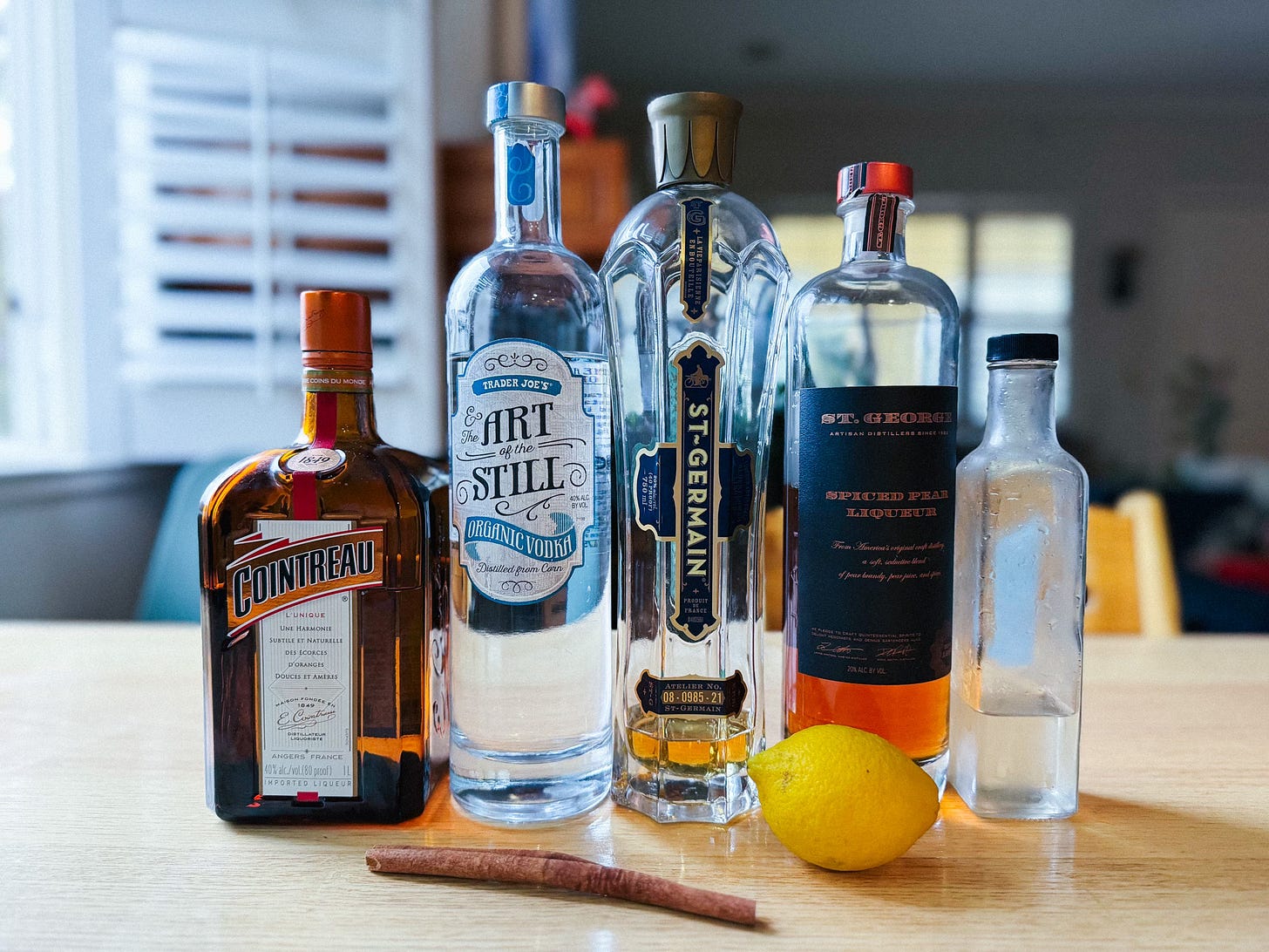 A bottle of Cointreau, vodka, St Germain elderflower liqueur, St. George Spiced Bear Liqueur, simple syrup, lemon, and cinnamon stick