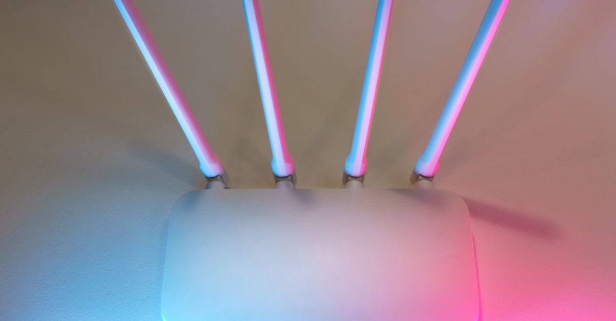 Photo: Jakub Zerdzicki / Pexels Sleek white wireless router with four antennas emitting soft blue and pink light.