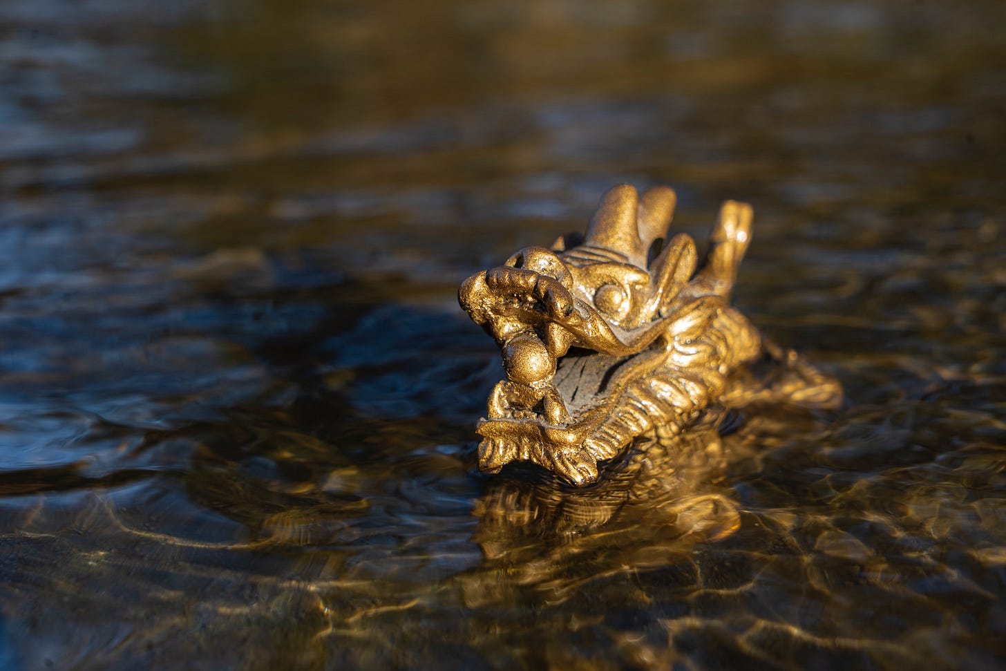 Fotografia em cores de uma escultura dourada de um dragão chinês, a escultura está saindo de um corpo d'água em movimento. O dragão tem uma bola na boca. Fotografia em cores de uma escultura dourada de um dragão chinês, a escultura está saindo de um corpo d'água em movimento. O dragão tem uma bola na boca.