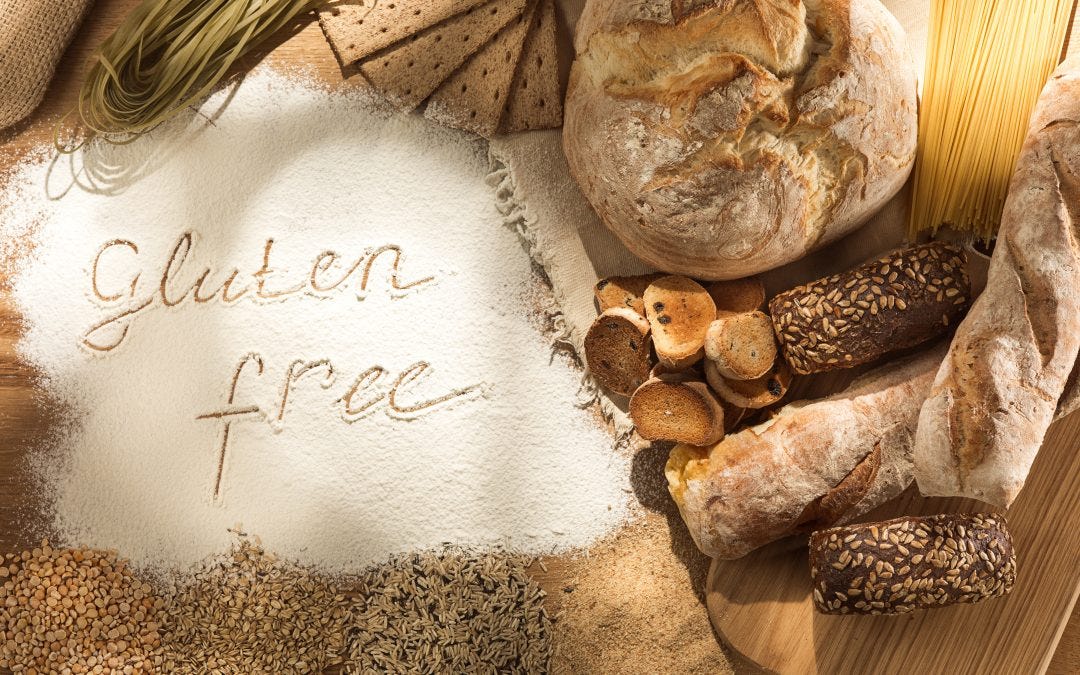 Bread and snacks on wood. Flour spread on the wood with the words "gluten free" drawn out in cursive.