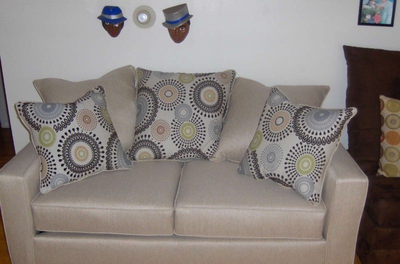 Beige couch with multi-colored pillows next to dark brown pillows and a ceramic set of faces