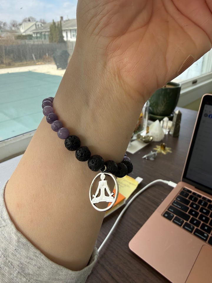Two bracelets with lavender colored stones and lava rock. One has a shiny bead and the other a yoga charm.