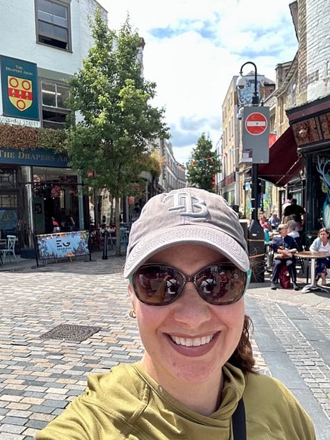White woman poses awkwardly in front of cathedral and gardens