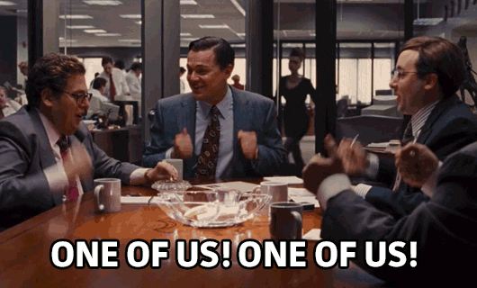 A gif of four white guys in suits at a conference table chanting "One of us! One of us!" and banging on the table with their fists