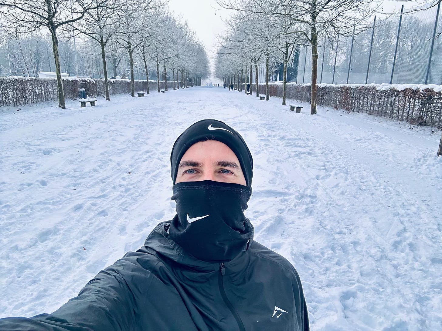 Runner in black Nike gear taking a selfie on a snow-covered park path lined with bare trees in winter Runner in black Nike gear taking a selfie on a snow-covered park path lined with bare trees in winter