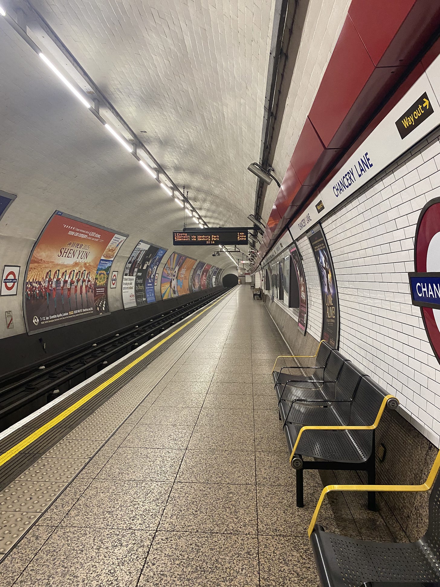 Full length of a platform at Chancery Lane station, taken from one end, with billboards and the track on the left and the platform on the right