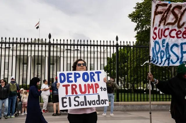 Woman holds sign that reads "Deport Trump to El Salvador" in front of White House