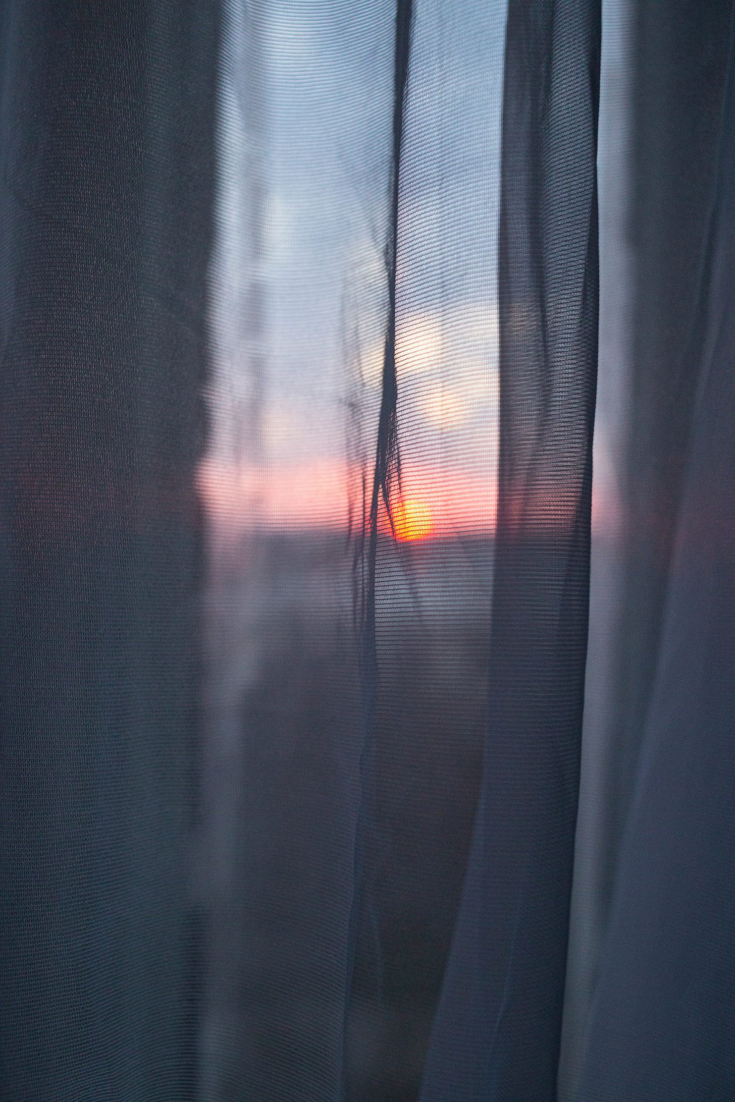 Soft dawn light seen through sheer curtains, with muted blues and a small glow of sunrise near the horizon. Soft dawn light seen through sheer curtains, with muted blues and a small glow of sunrise near the horizon.