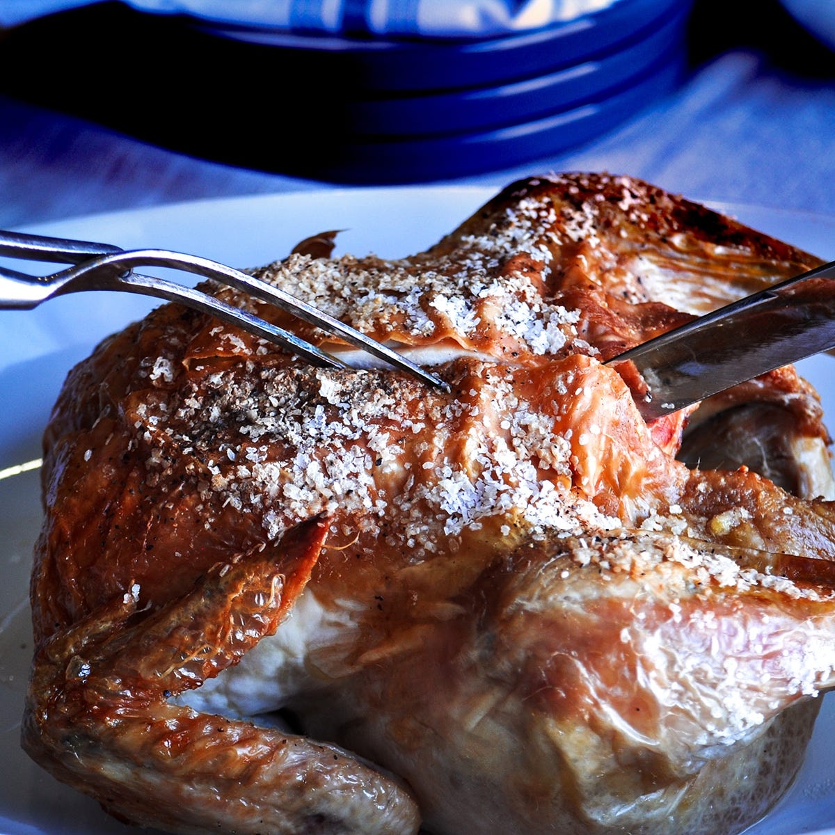 Someone using a knife to cut into a roast chicken with crispy skin.