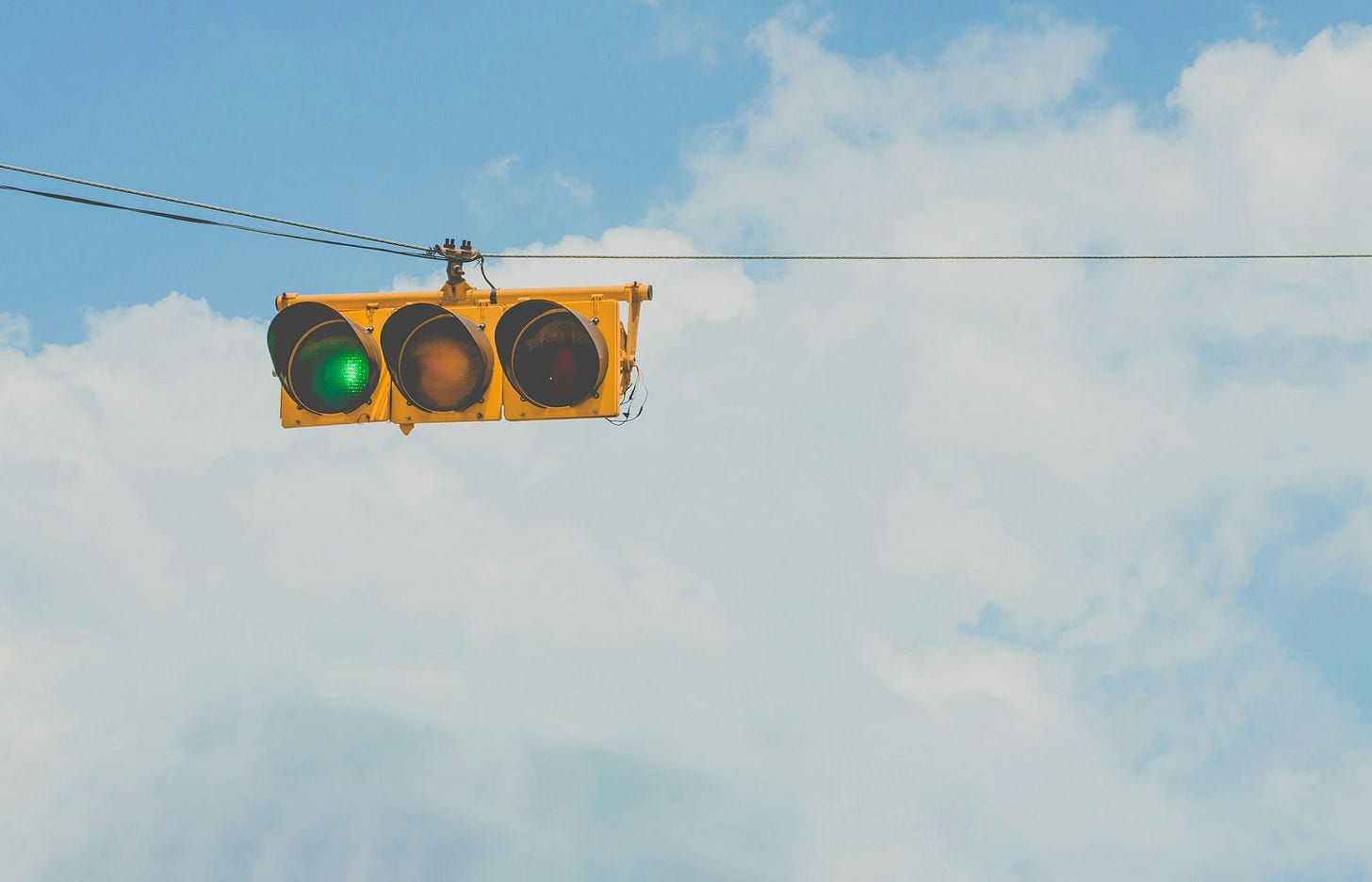 Cielo azzurro con nuvole bianche e in primo piano un filo orizzontale che regge un semaforo orizzontale giallo con il segnale di verde a sinistra, illuminato. Cielo azzurro con nuvole bianche e in primo piano un filo orizzontale che regge un semaforo orizzontale giallo con il segnale di verde a sinistra, illuminato.