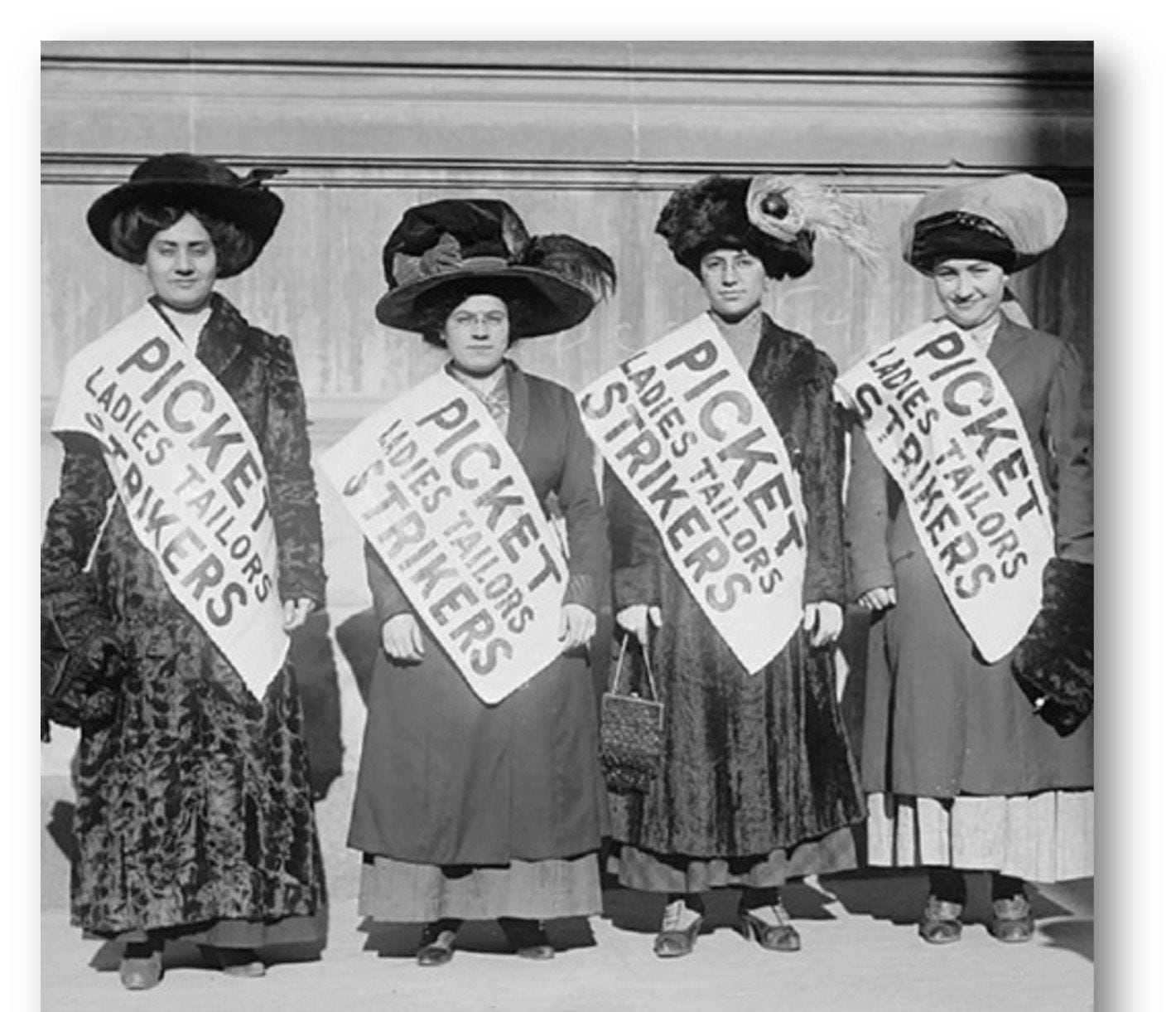 A photo of four women standing in a row looking at the camera. Black and white. They have big black hats on, olive, light skin and dark hair and are wearing large sashes that say "Picket Ladies Tailors Strikers" A photo of four women standing in a row looking at the camera. Black and white. They have big black hats on, olive, light skin and dark hair and are wearing large sashes that say "Picket Ladies Tailors Strikers"