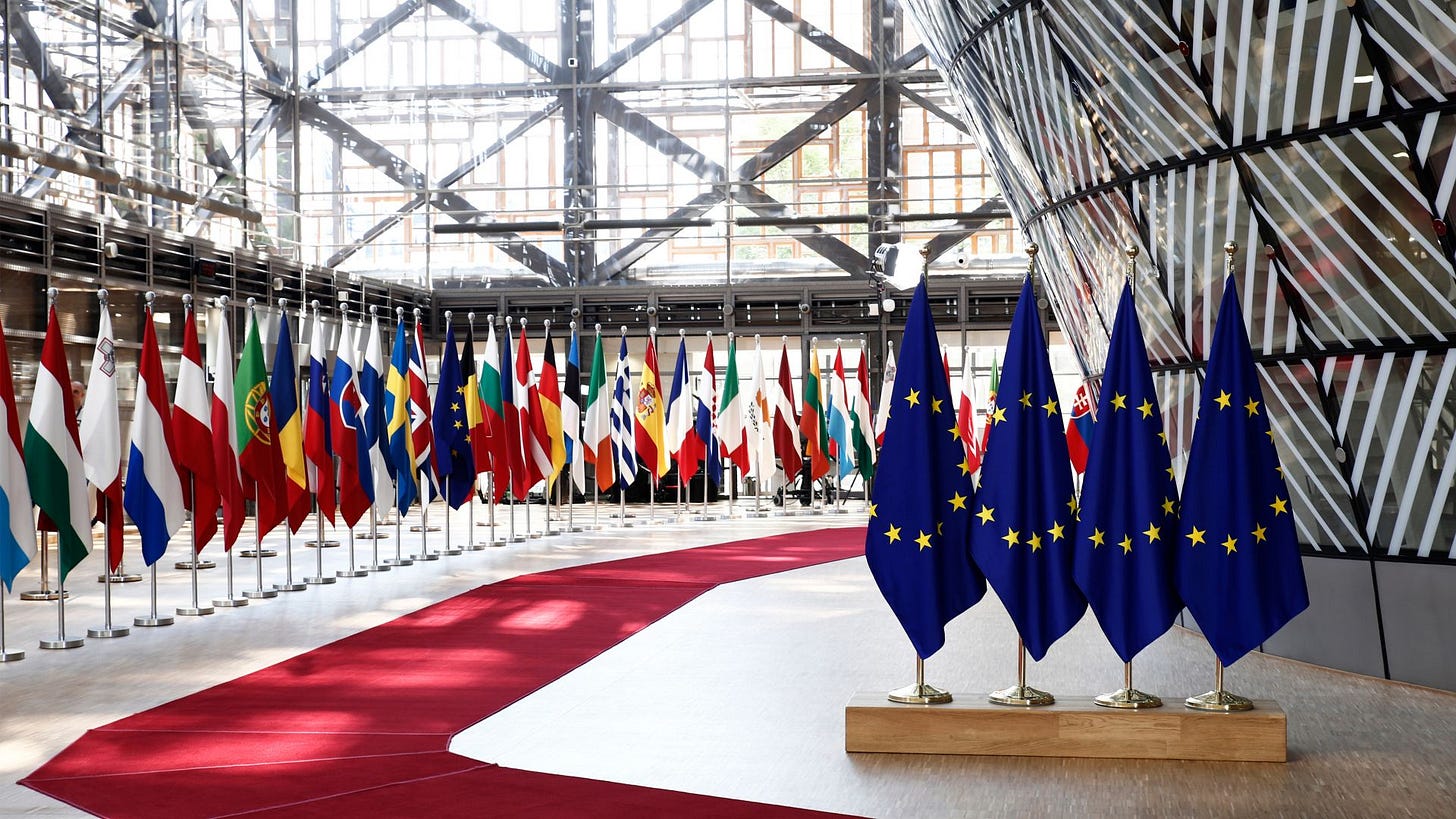 Interior of an EU institutional building displaying the European Union flag alongside national flags of member states.