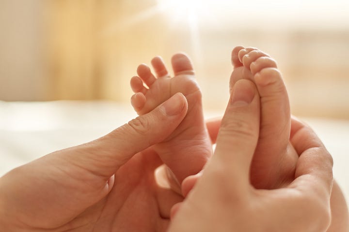 Hände halten Babyfüße und Baby hält sich an Fingern fest.