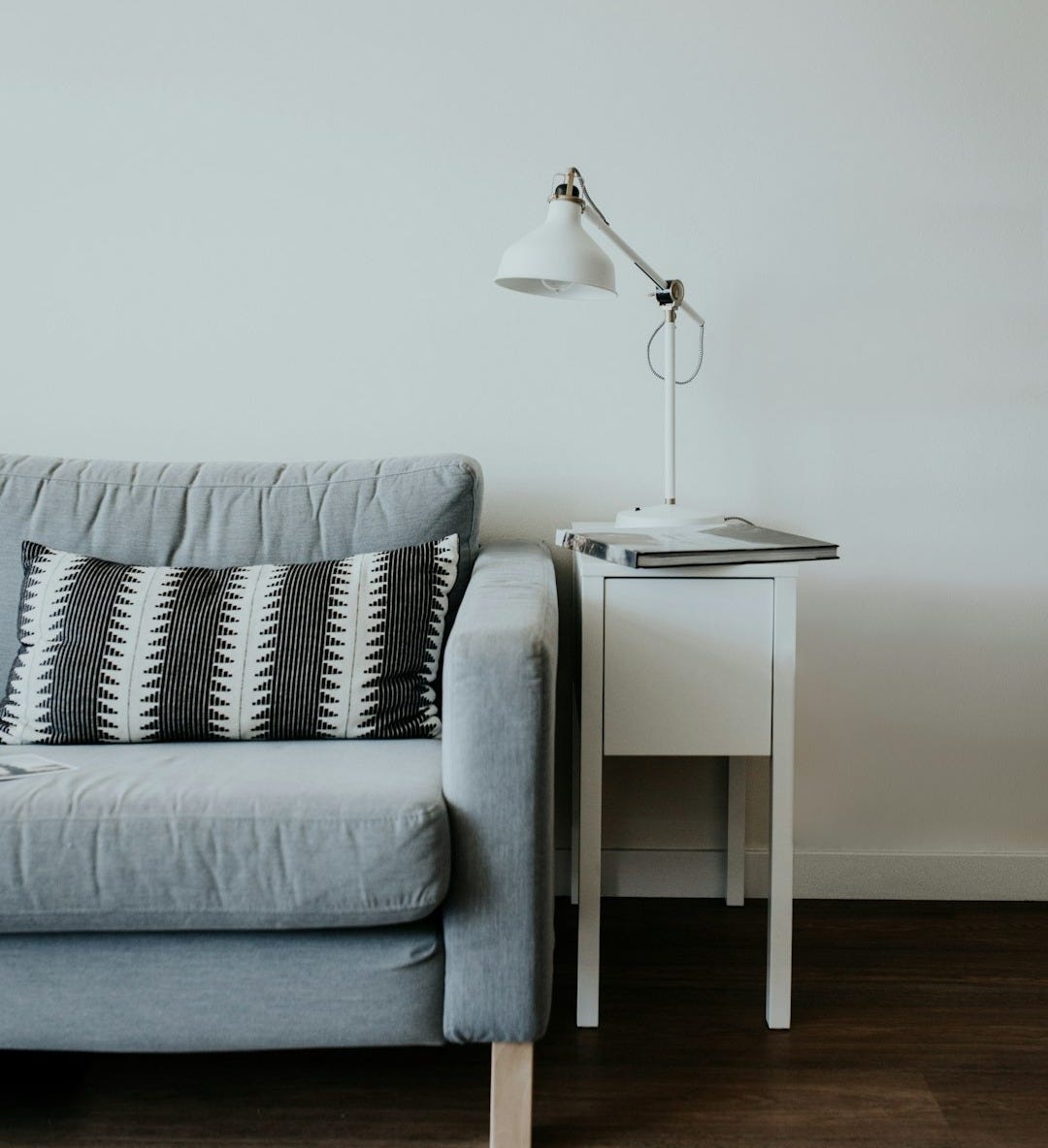 white study lamp on top of white wooden end table beside gray fabric sofa white study lamp on top of white wooden end table beside gray fabric sofa