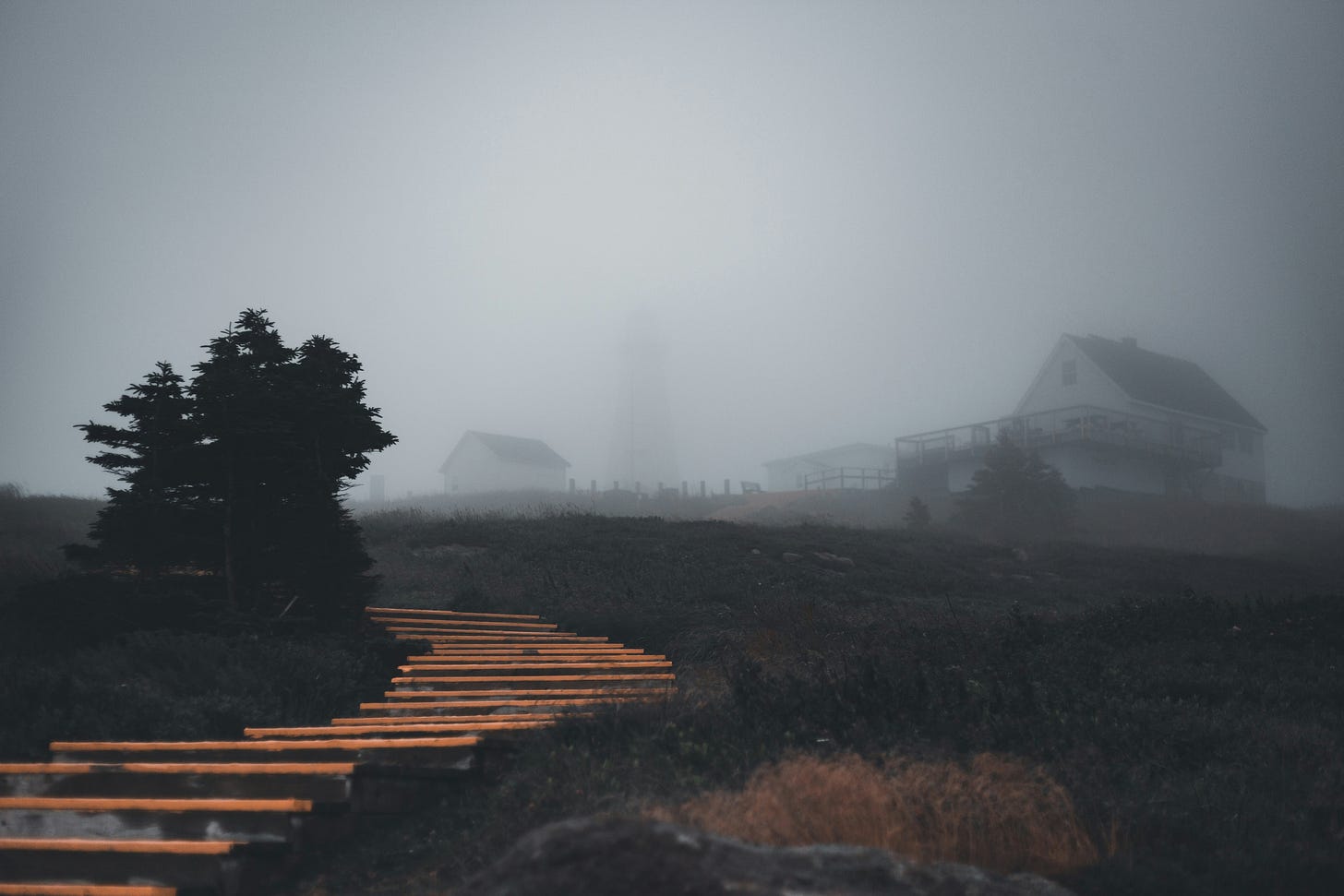 A little house is enveloped in fog, a brighter path to the house can be seen in the foreground.