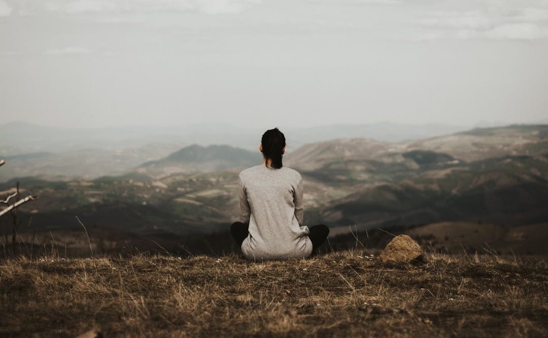 woman sitting on cliff overlooking mountains during daytime
