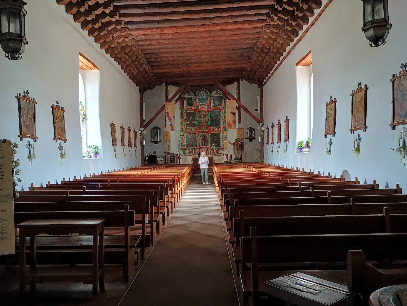 Interior of old church with wooden log ceiling, huge colorful altarpiece, and woman walking up aisle between wooden pews