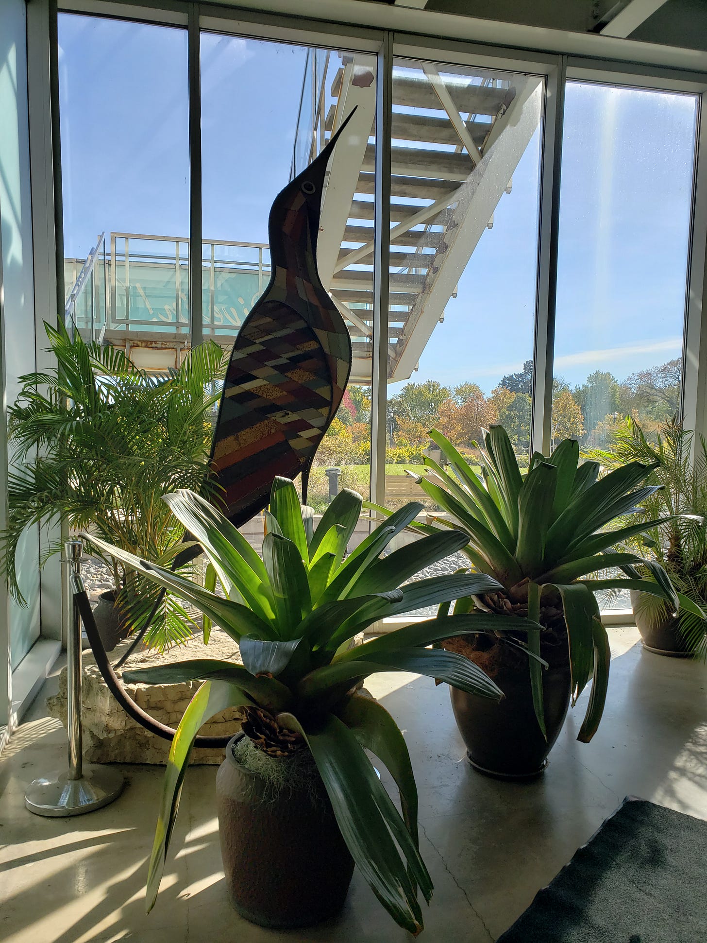 A large stained glass bird art piece nestled in with some large plants in the Visitor Center.