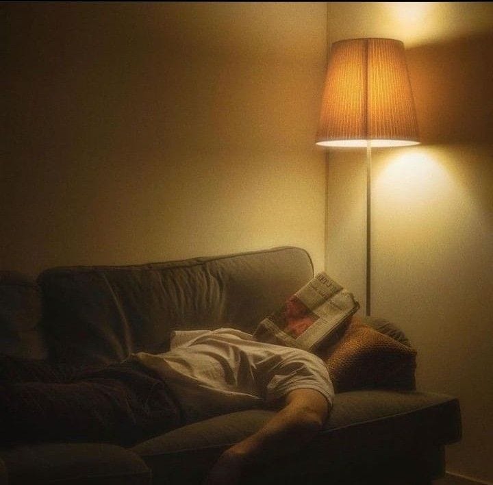 This may contain: a man laying on a couch under a lamp