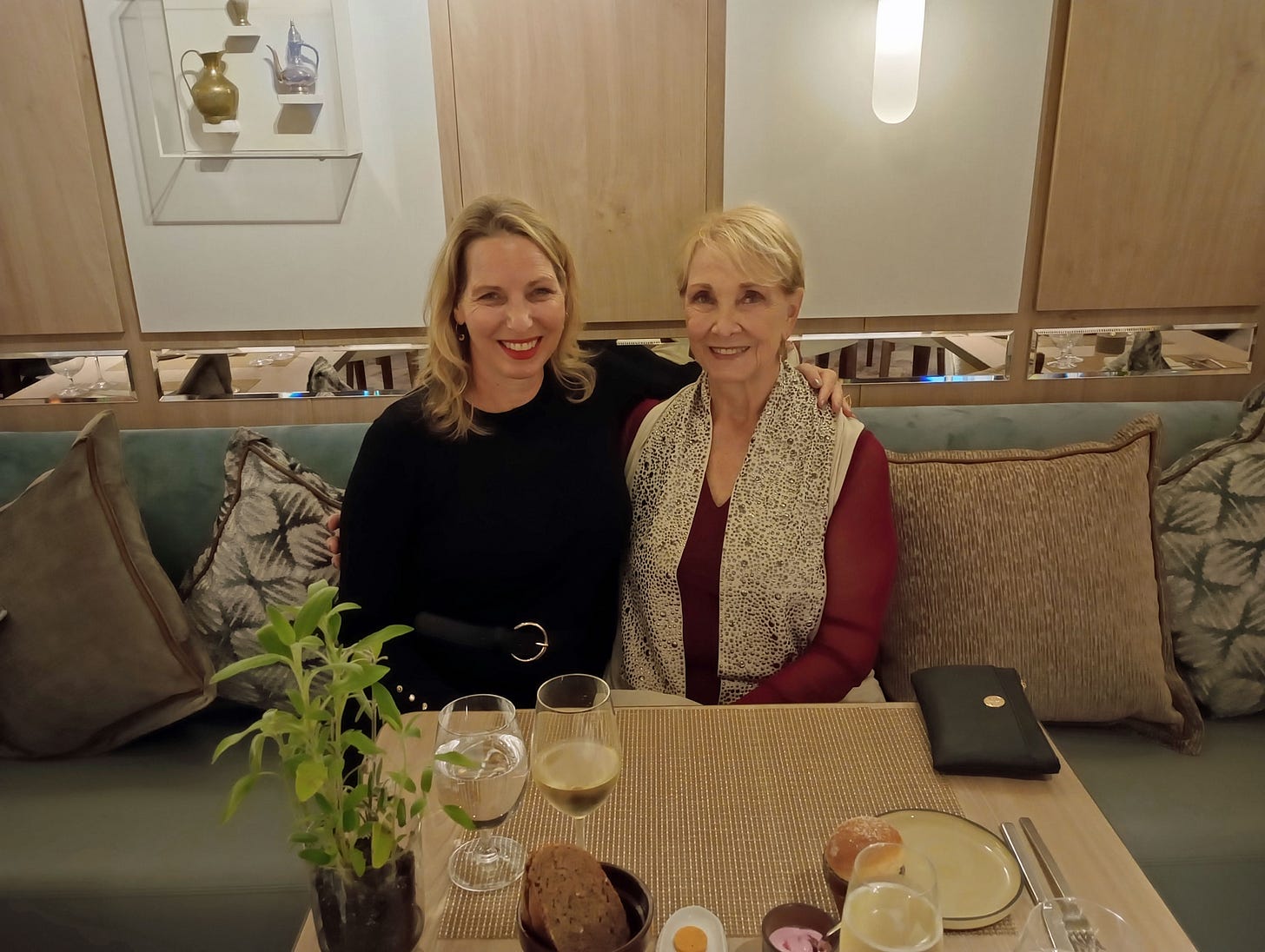 Two white women with blond hair, motther and daughter, sit at a dining table. The younger woman has her arm around her mother.