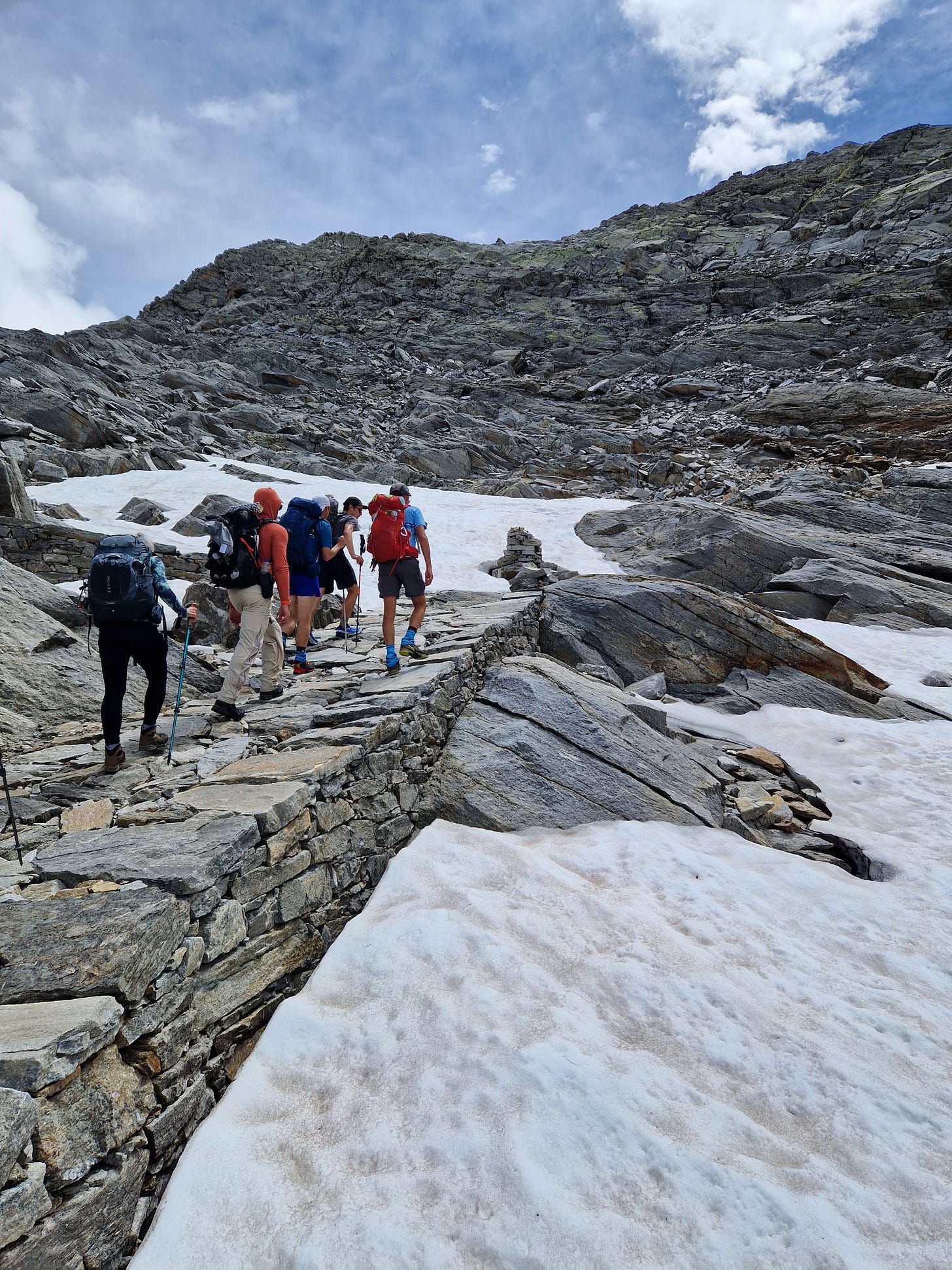 Hikers walking up a rocky path near to snow patches Hikers walking up a rocky path near to snow patches