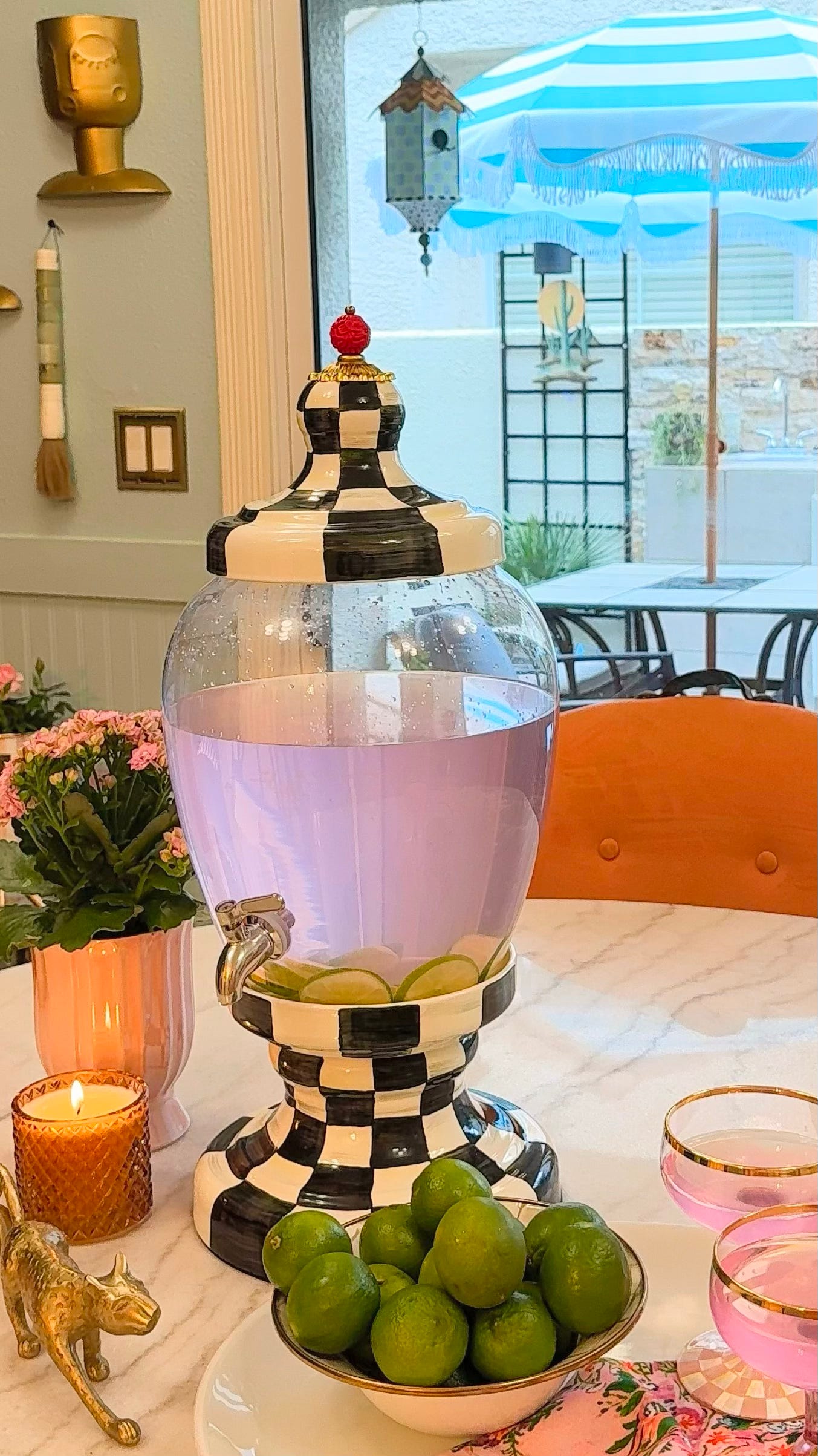 MacKenzie-Childs Courtly Check Beverage Hostess filled with a pink citrus drink on a marble kitchen island in Shaunda Necole's Las Vegas home. Styled by The Soul Food Pot® with fresh flowers, candles, and entertaining accents celebrating Southern hospitality and whimsical home decor.