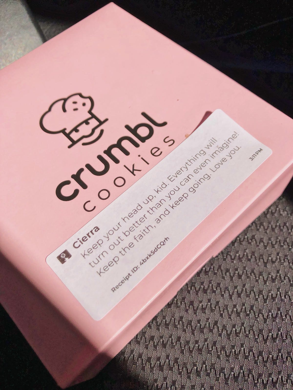 A closed Crumbl Cookie box with an encouraging and loving note sticker on top