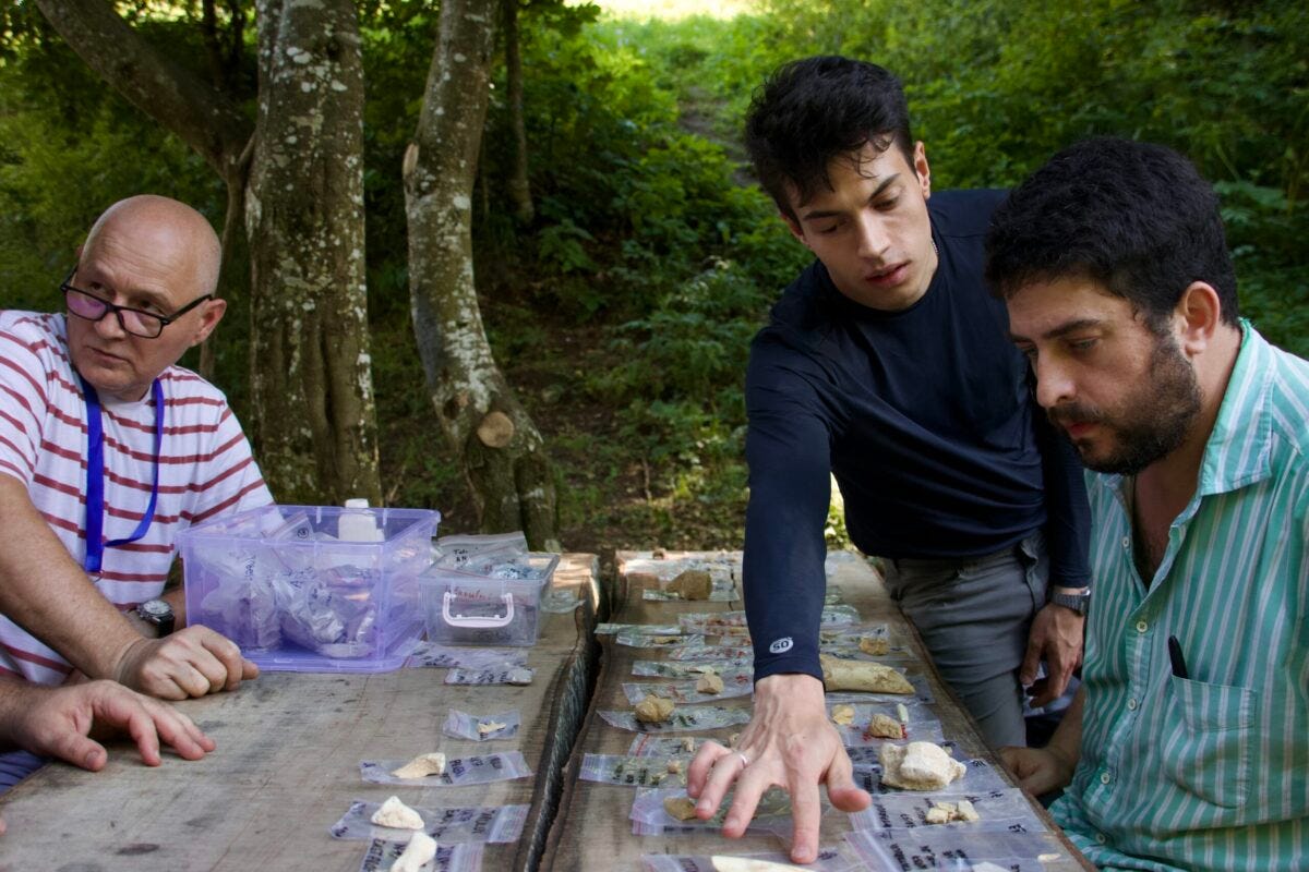 Pesquisadores analisam fragmentos de ossos achados durante a expedição, colocados sobre a mesa de um parque. À direita, o professor André Strauss e o aluno de mestrado Victor Nery, do MAE-USP. À esquerda, o professor Marian Cosac, da Universidade Valahia de Târgoviște - Foto: Herton Escobar / USP Imagens