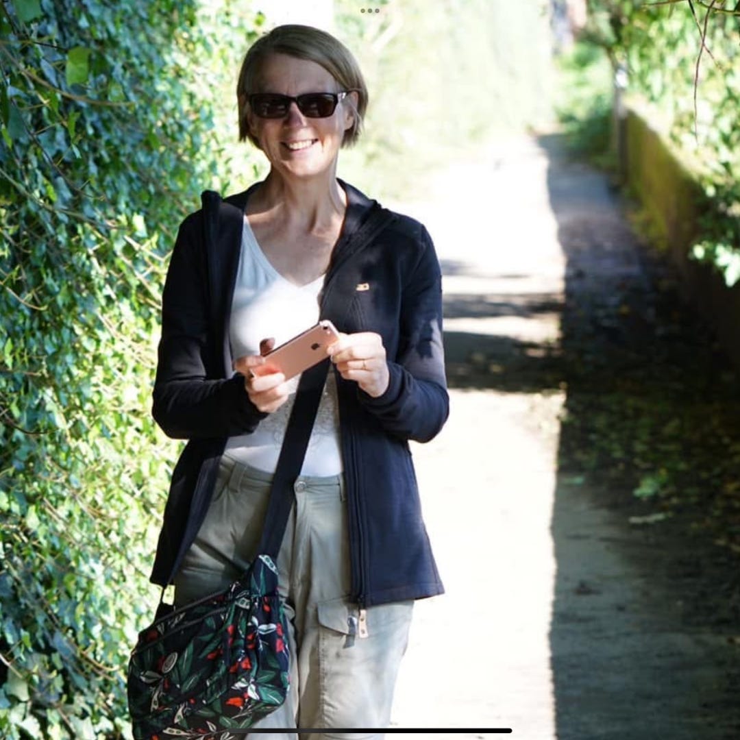 Photo of the author walking along a country path on a sunny day. She is smiling and wearing sunglasses.