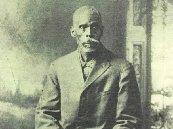 A black and white photo of a dark-skinned Black man wearing a suit. The photo was taken in the 1900s. A black and white photo of a dark-skinned Black man wearing a suit. The photo was taken in the 1900s.