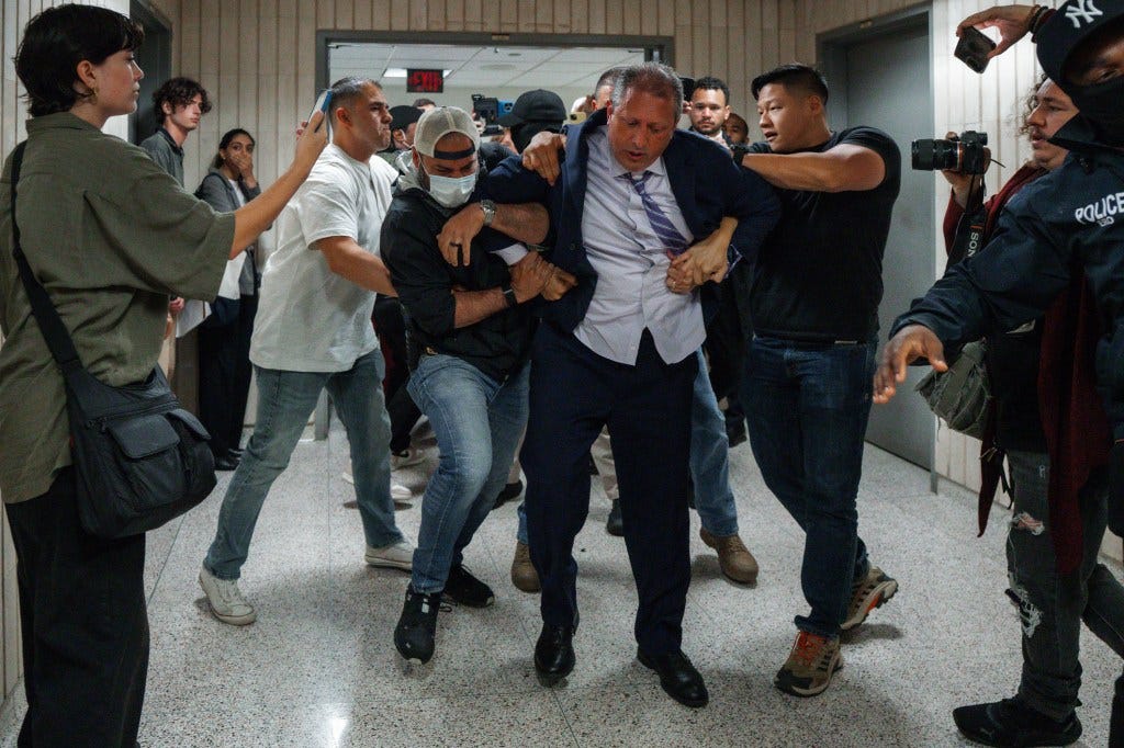 A man in a suit being arrested by law enforcement in a hallway.