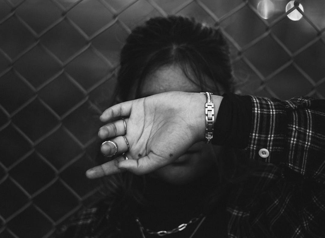 a black and white photo of a person covering their face behind a fence