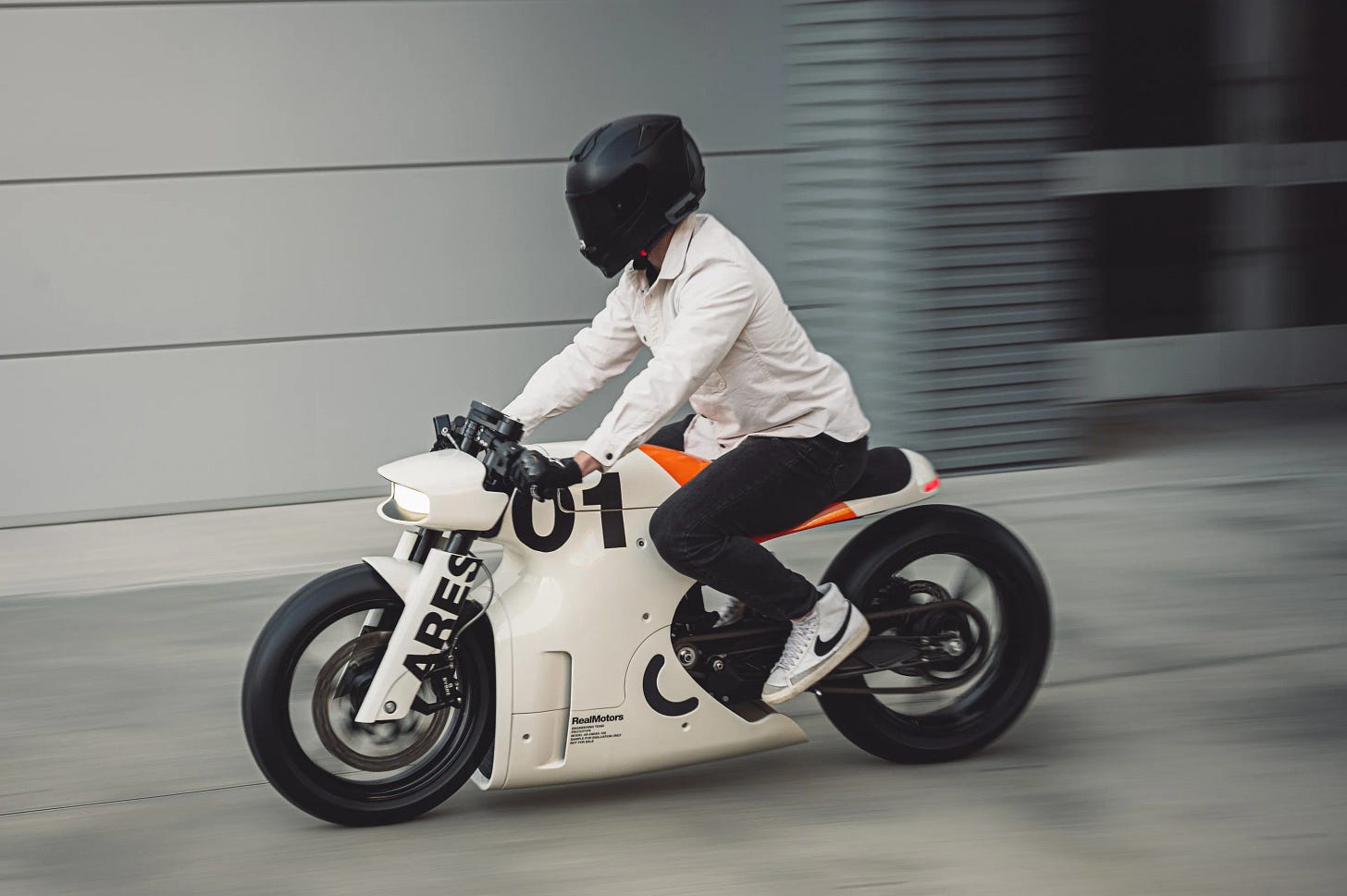 Person riding fast on an electric cafe racer motorcycle.
