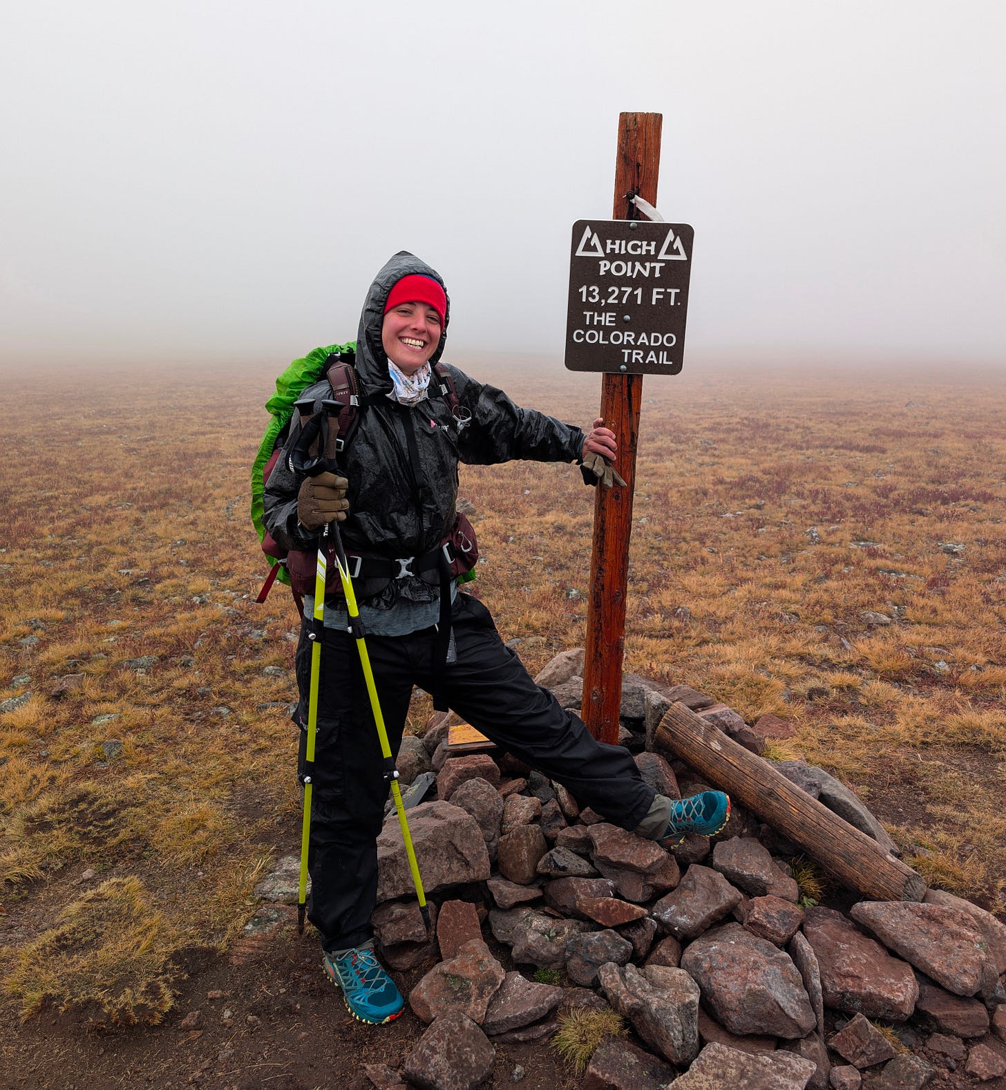 Smiling hiker in rain gear posing beside the Colorado Trail High Point sign, 13,271 ft, in foggy weather. Smiling hiker in rain gear posing beside the Colorado Trail High Point sign, 13,271 ft, in foggy weather.