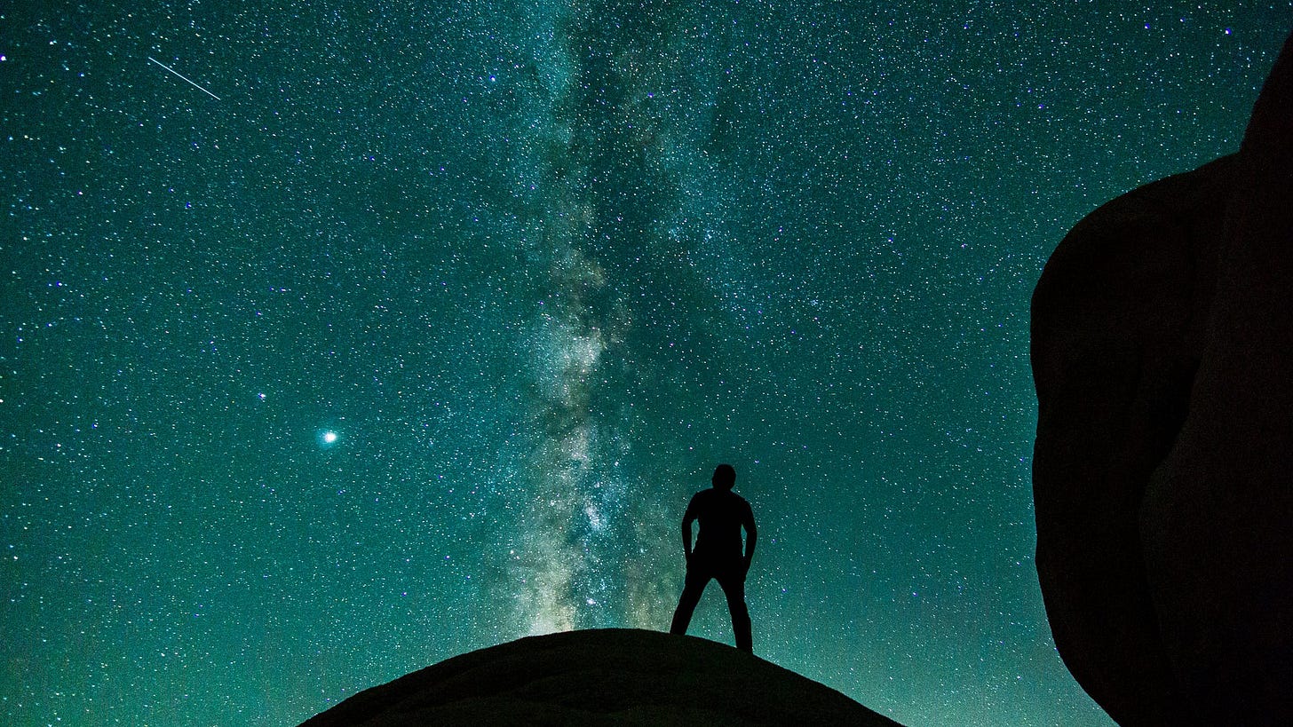A person stands on a hill gazing at the stars and the heavens