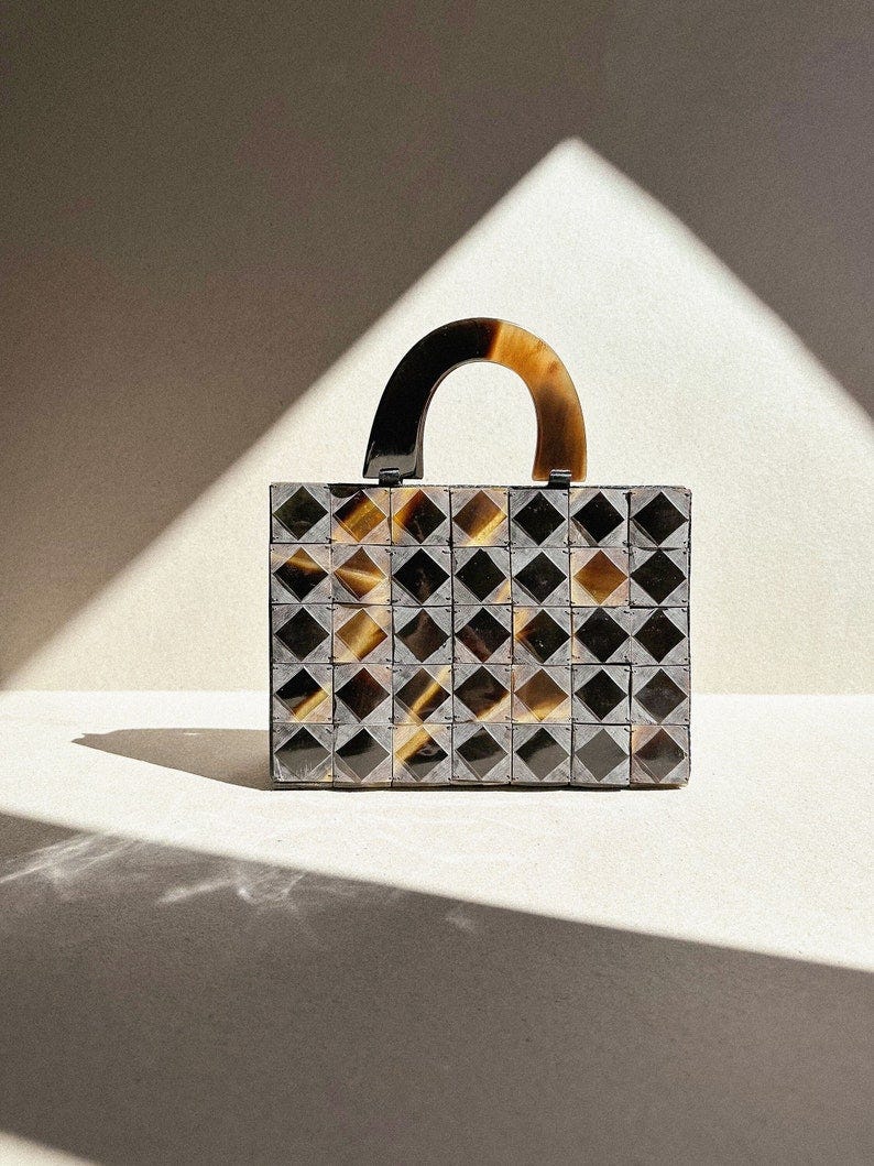 May include: A small, black and brown geometric patterned handbag with a tortoiseshell handle.