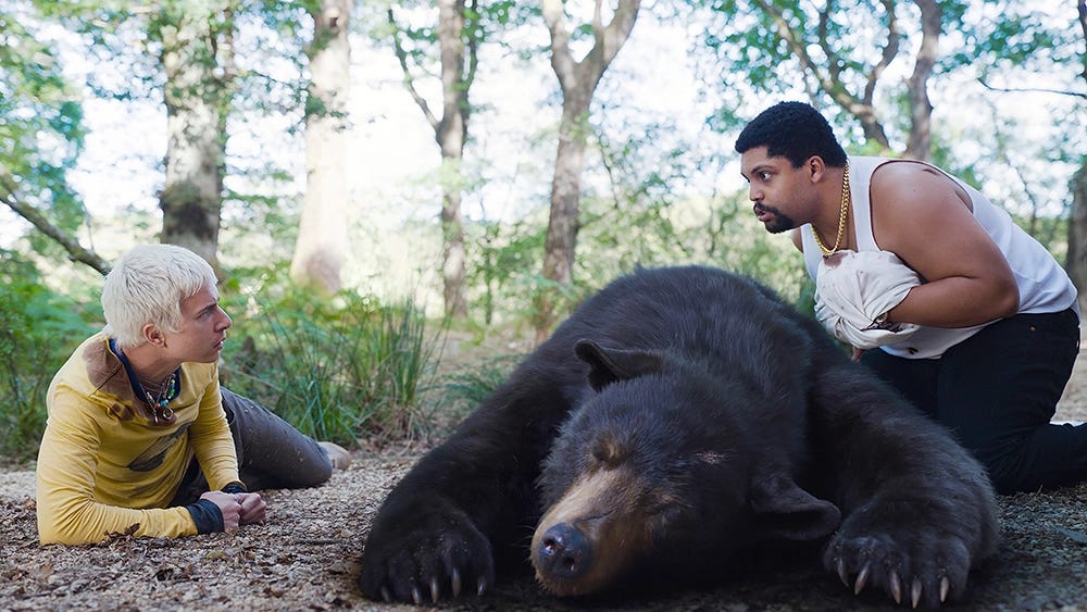 Stache and Daveed around the bear, which has collapsed on Eddie.