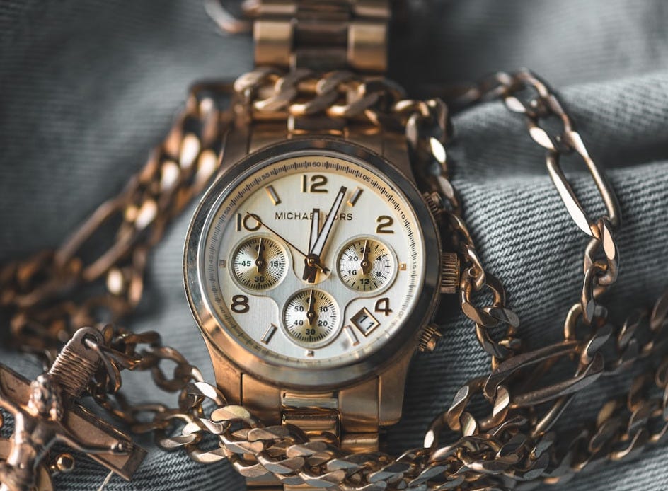 round gold-colored Michael Kors chronograph watch with link band on blue denim