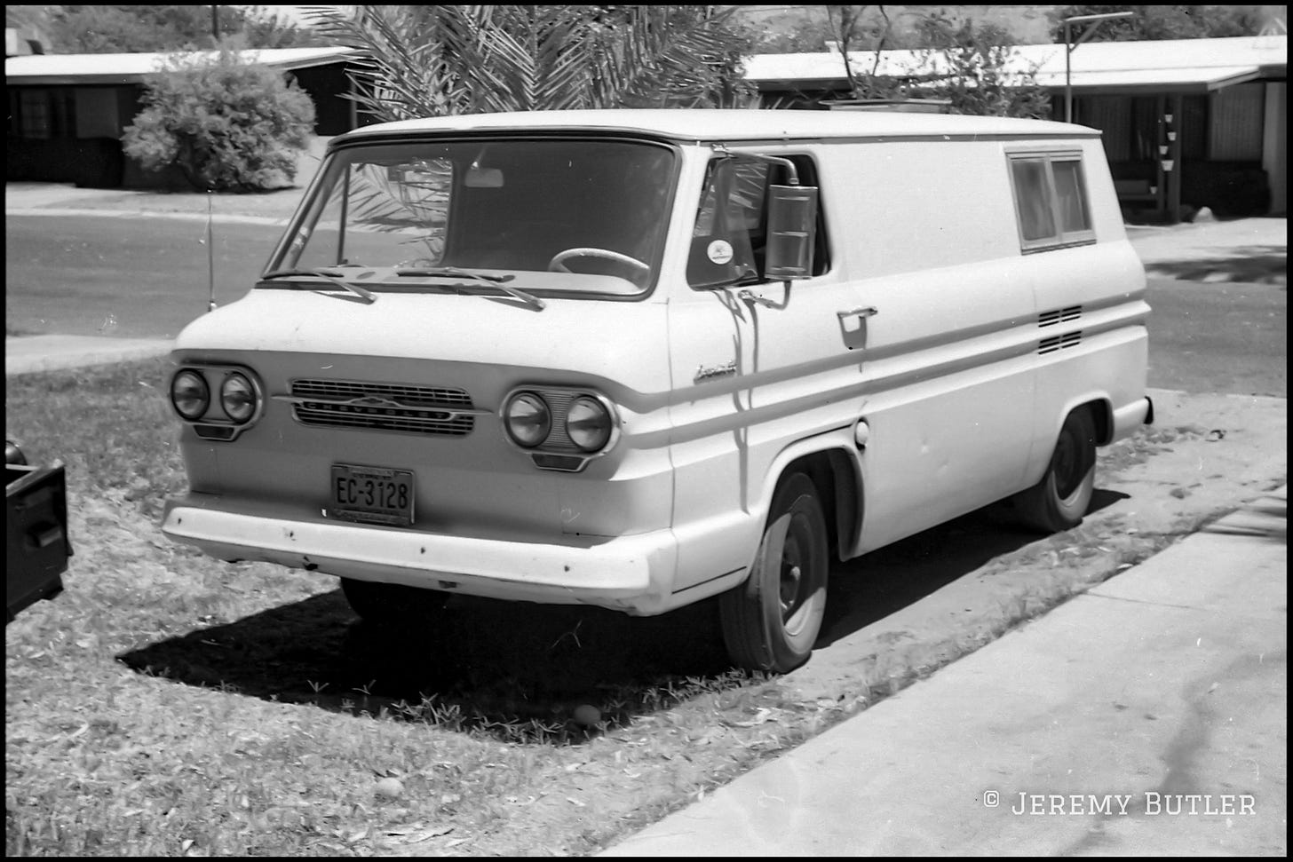 Black and white photo of a vintage Chevrolet Corvair 95 panel van parked on grass near a sidewalk.