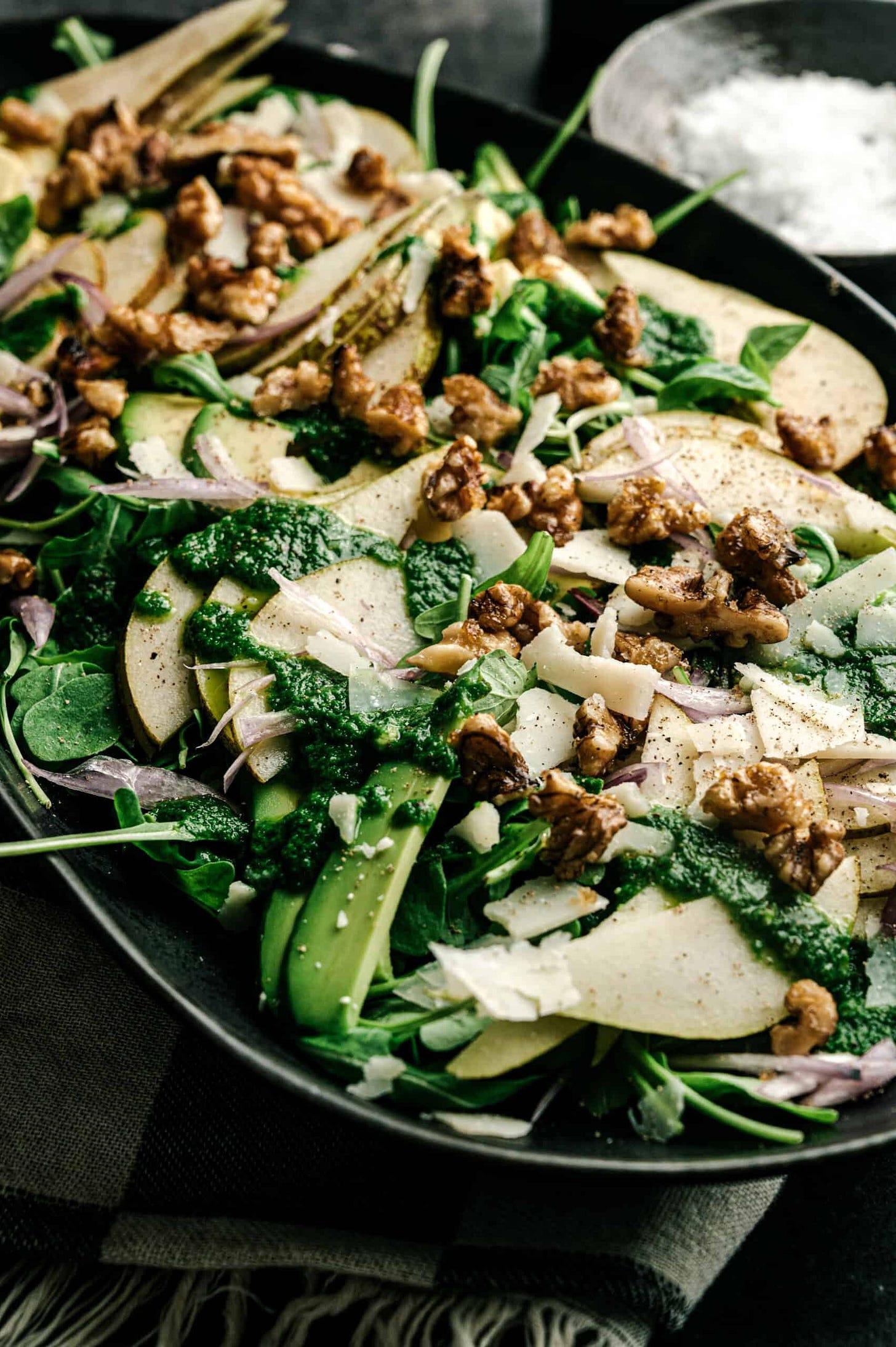 close-up of an avocado pear salad featuring arugula, candied walnuts, and basil-lime dressing. 