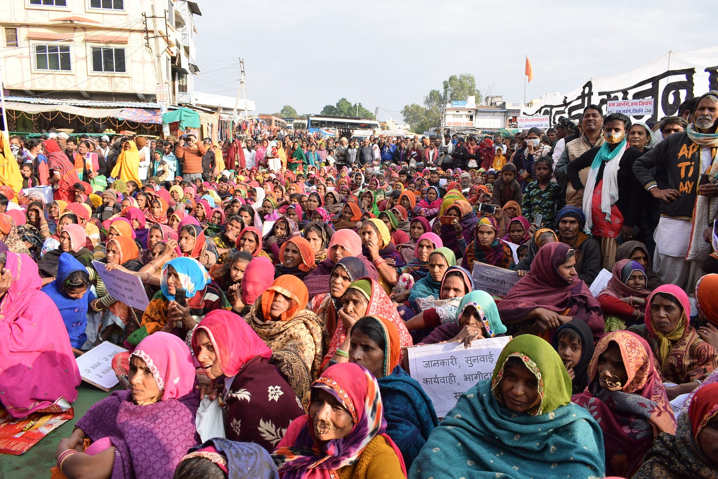 A large group of people in a rural setting, sitting on the ground and listening to something at an event A large group of people in a rural setting, sitting on the ground and listening to something at an event
