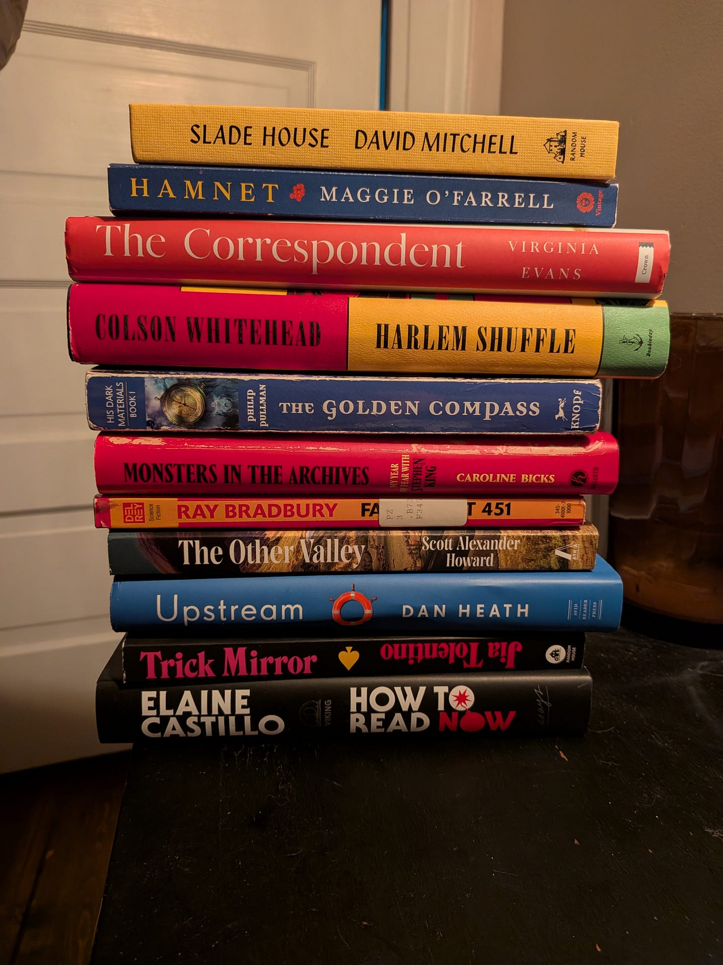 A stack of books: Slade House, Hamnet, The Correspondent, Harlem Shuffle, The Golden Compass, Monsters in the Archives, Fahrenheit 451, The Other Valley, Upstream, Trick Mirror, How to Read Now