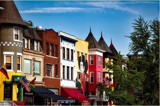 Brightly colored rowhouses on a sunny day with a mural showing a cowboy painted on them and American flags hanging outside Brightly colored rowhouses on a sunny day with a mural showing a cowboy painted on them and American flags hanging outside