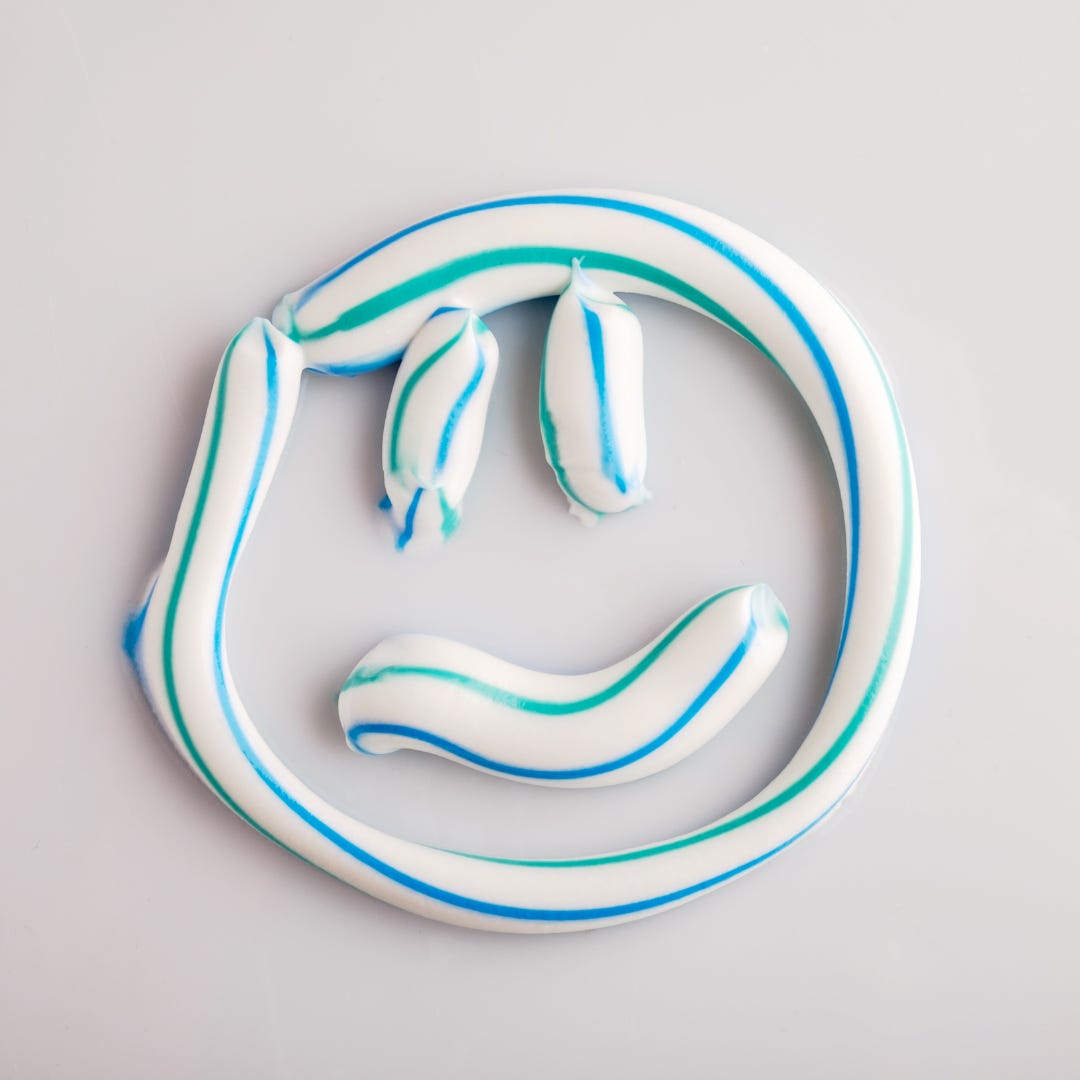A photo of toothpaste squirted into a smiley faced shape. The toothpaste is white with green and blue stripes.
